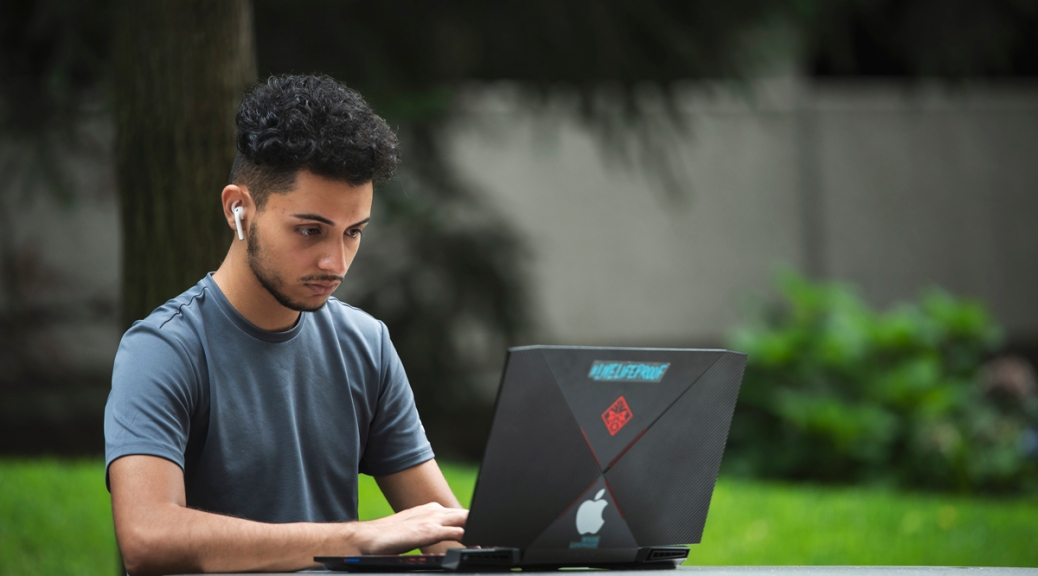 A student works on a laptop at a table on the Student Plaza